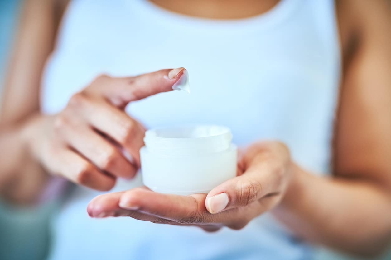Woman dipping her finger into a container of skincare lotion