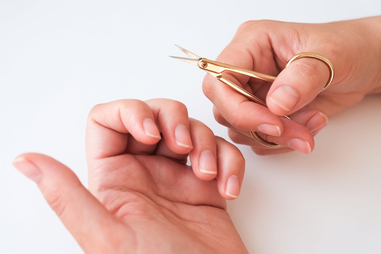The woman is cutting her nails with small scissors by herself in close up photo on white background. View from above. Manicure at home