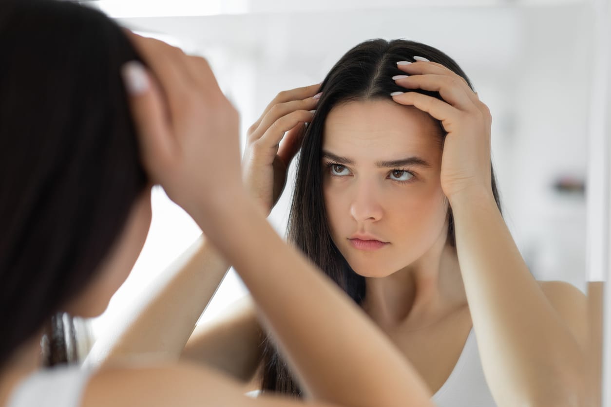 Young woman examining her scalp in the mirror