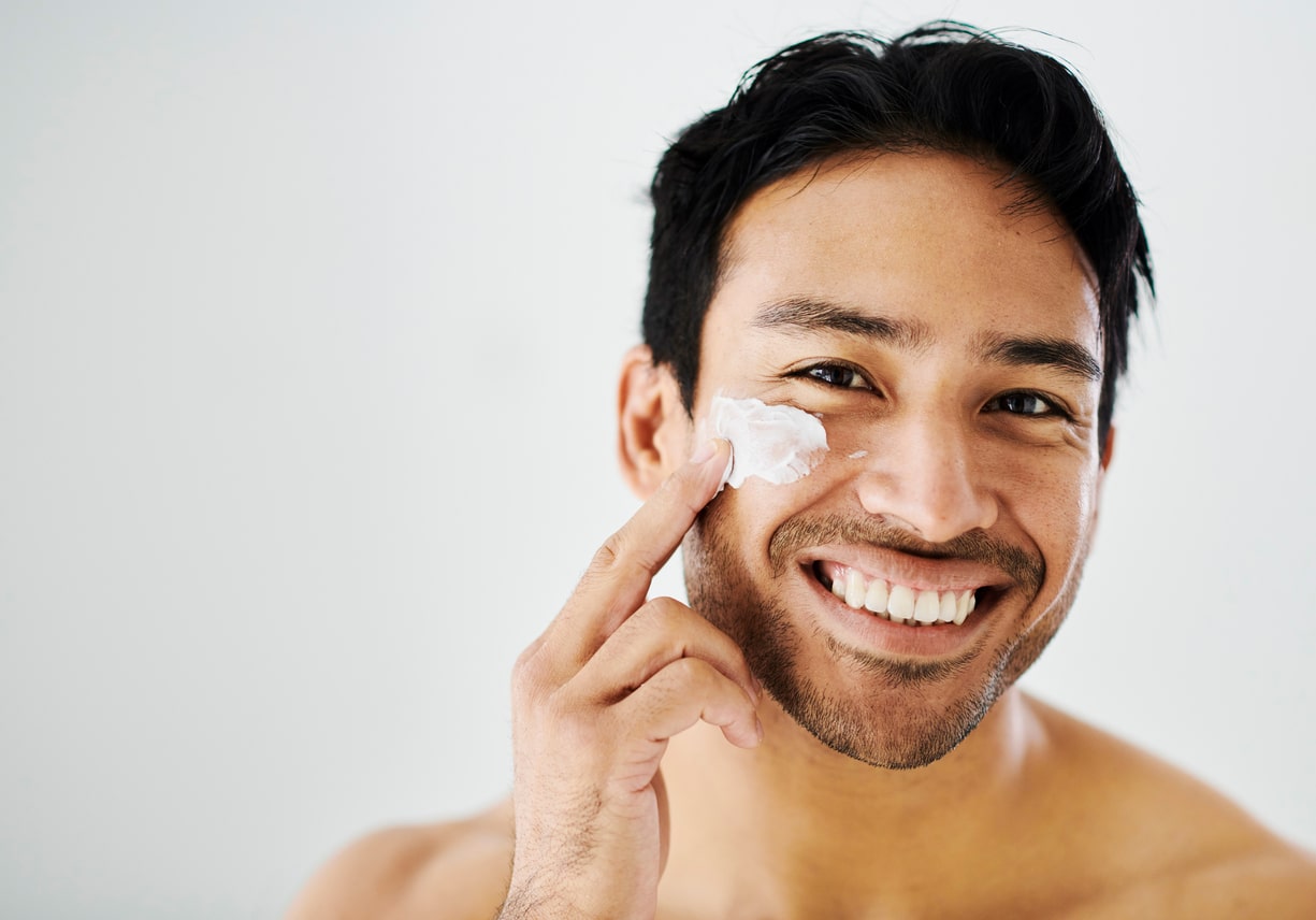 Face cream and beauty of a man with healthy skin, applying moisturizer for good hygiene. Routine skin care by a bare handsome male, applying lotion. A happy guy feeling fresh in the morning