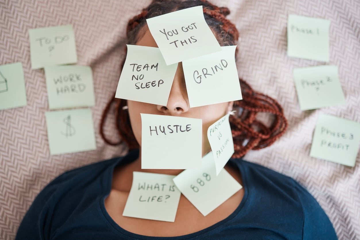 Tired, sticky note and sleeping woman in overworked, schedule or overwhelmed with work and tasks on bed. Female worker covered in paper, pressure and bedroom chaos or information overload at home